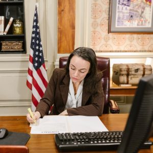 Female attorney in a law office signing legal documents at her desk, surrounded by legal books and symbols of justice.
